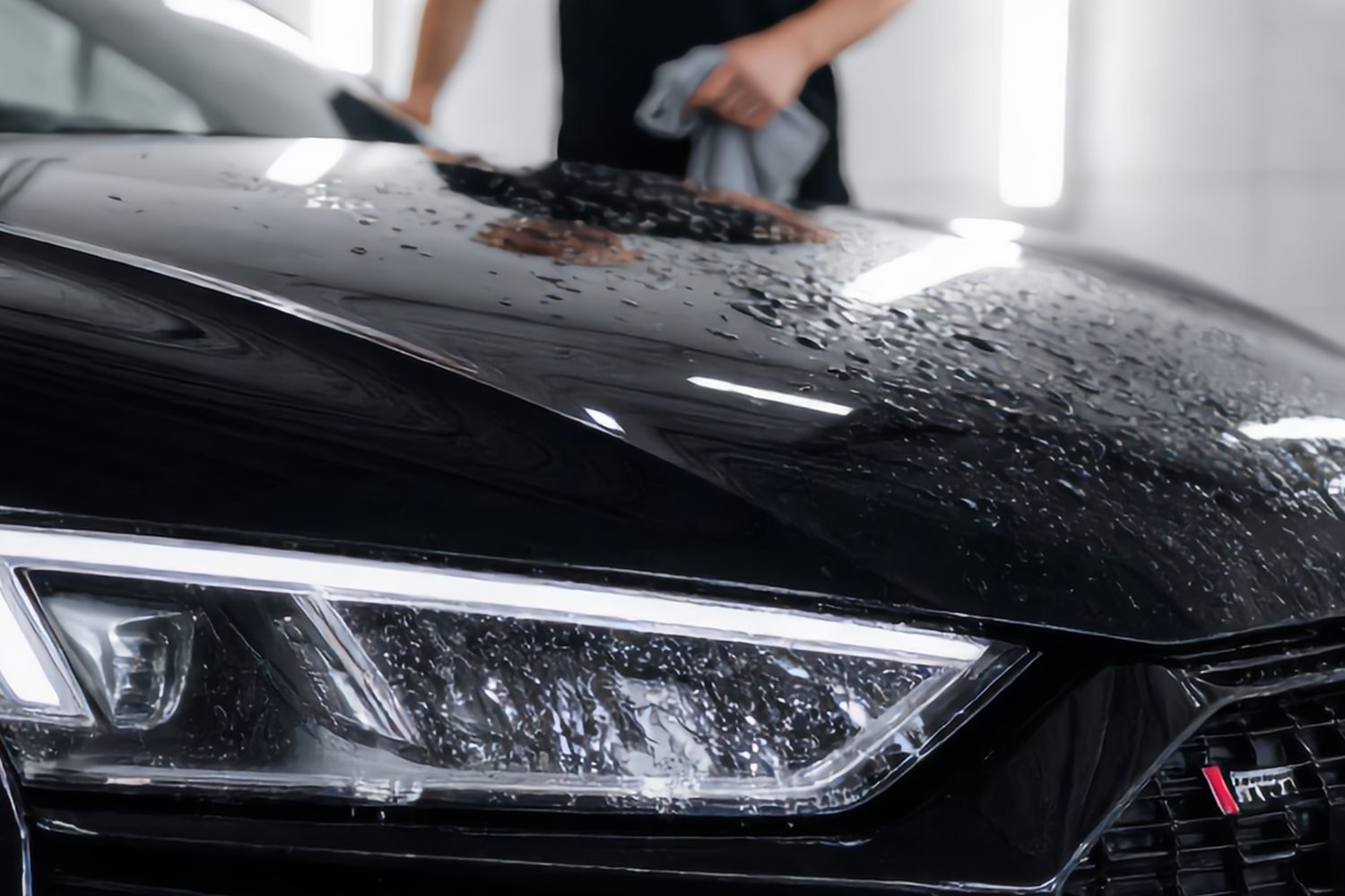Close-up van water dat in dikke druppels op de gecoate motorkap en koplamp van een zwarte Audi R8 blijft staan